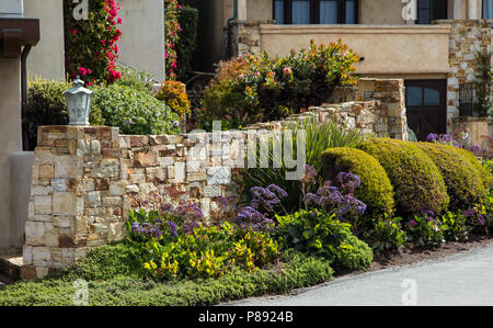 Home landscaping example with a garden wall featuring intricate stone work and a varied palette of planting Stock Photo