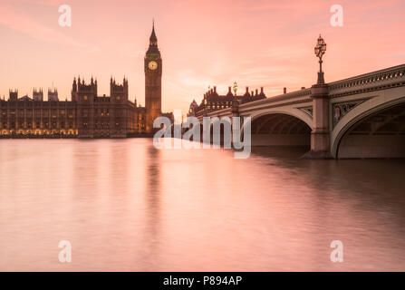 Orange sunset over Big Ben and the Houses of Parliament in London including Westminster Bridge reflected in the smooth water of the River Thames Stock Photo