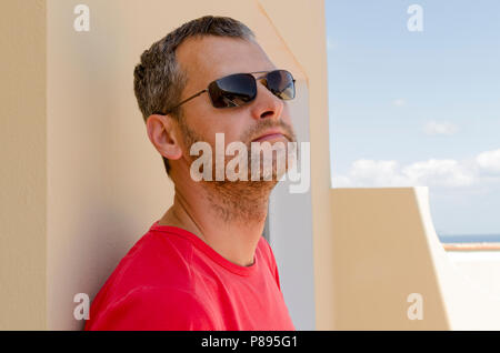 A portrait of a middle aged thoughtful man in sunglasses leaning against the wall Stock Photo