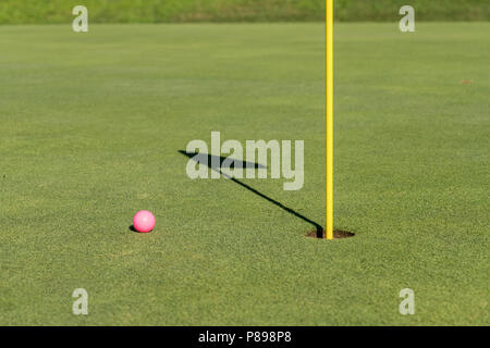 Pink golf ball by flag and hole on putting green Stock Photo