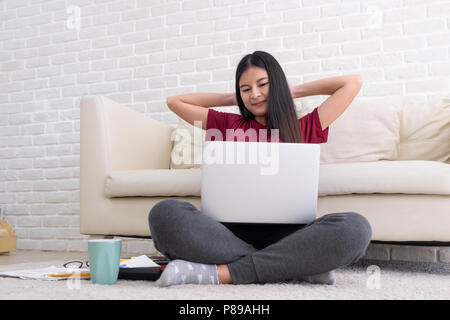 Asian woman freelance raise arm and rest at back of head and close eye in front of laptop computer in living room at home,relax from hard work.work at Stock Photo