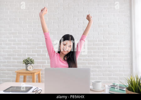Asian woman freelancer raise arm up stretching in front of laptop on desk from work in home office,work at home Stock Photo