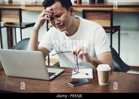 asia casual man cover face with hand upset from work in front of laptop computer in coffee shop,stress emotion concept,work outside office,work at hom Stock Photo