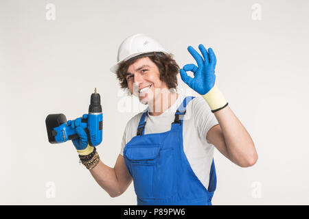 Studio portrait of happy builder laughing at camera with screwdriver wearing gloves and white helmet Stock Photo