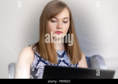Pretty young woman with red hair wearing blue dress working on laptop computer Stock Photo