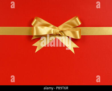 Gold gift bow ribbon horizontal isolated on red wrapping paper background Stock Photo