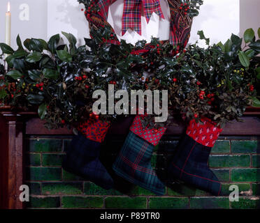 Home made Christmas stockings hanging on a mantelpiece with a garland of fresh holly Stock Photo