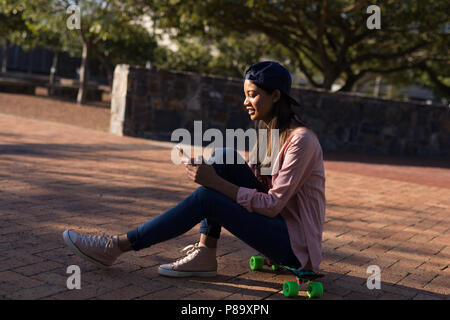 Woman sitting on the skateboard using mobile phone Stock Photo