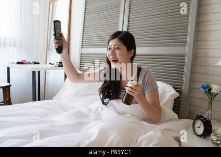 Asian woman sitting in her bed and raised up her hands in the air to cheer for her favorite basketball team. Stock Photo