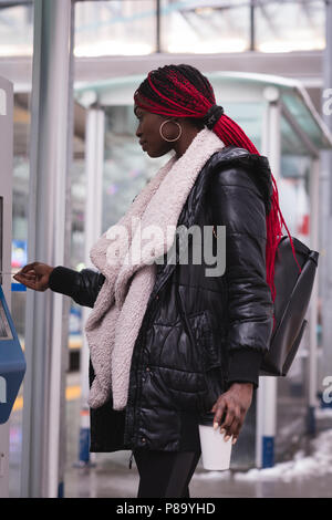 Young stylish woman using a ticket punching machine in public transport ...