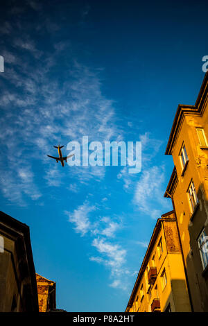 Passenger jet plane is flying over street in downtown Sofia, Bulgaria. Blue sky with some white clouds, old brown brick residential buildings, image taken at sunset