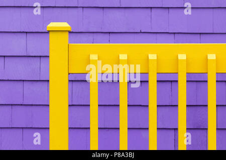 Purple shingle wall with yellow wooden fence.  Decorative minimalist background in complimentary colours. Stock Photo