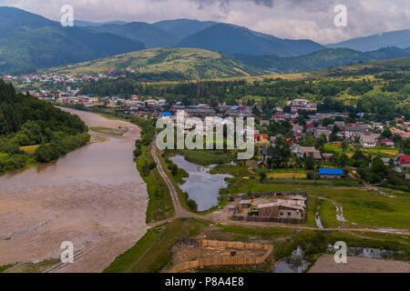 A stormy mountain river with dirty water flows near the village with small houses between the mountains . For your design Stock Photo