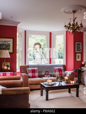 Checked cushions on brown leather sofa at bay window in Regency home Stock Photo