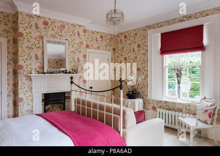 Bright pink blanket on metal framed bed in Regency home with Sanderson’s Summer Tree wallpaper Stock Photo