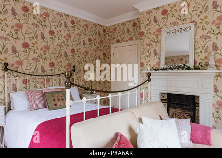 Bright pink blanket on metal framed bed in Regency home with Sanderson’s Summer Tree wallpaper Stock Photo