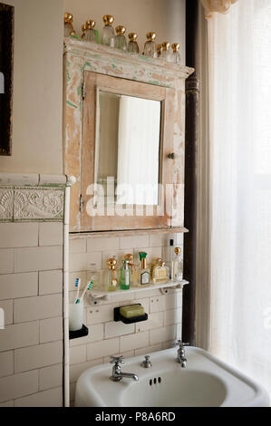 Old perfume bottles lined up along reclaimed mirrored cabinet in shabby chic bathroom Stock Photo