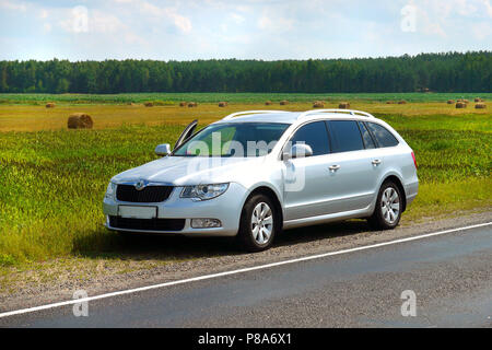 The silver car stopped on the side of the road near a large field with stacks of mown hay . For your design Stock Photo