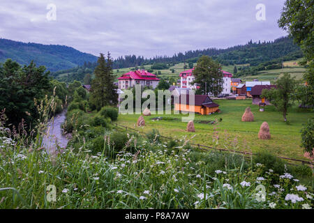 cottages for recreation on a green meadow with haystacks in a mountain valley against the backdrop of green mountain peaks and a cloudy sky. a place f Stock Photo