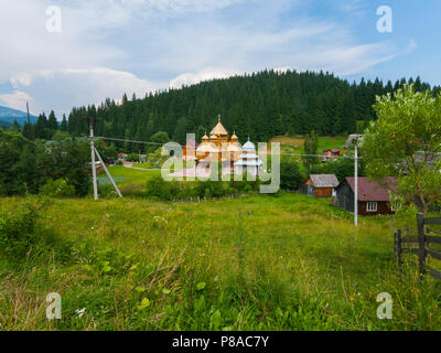 The picturesque green nature of a small mountain village with a power transmission line houses a church in the middle and a dense high forest. . For y Stock Photo