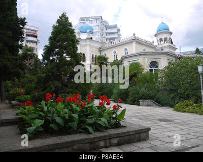 Flowerbed with red flowers on a background of green fir trees of beautiful hotel buildings . For your design Stock Photo