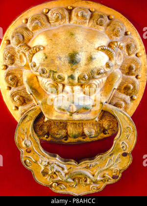 Ancient golden Chinese doorknob in the shape of a lion on a red vibrant door Stock Photo