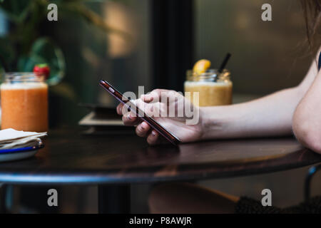 Crop hands of young female browsing modern smartphone while spending time at table in cozy cafe Stock Photo