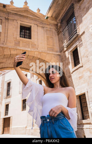 Charming young female in casual outfit posing for selfie while standing on amazing street of Valencia on sunny day Stock Photo