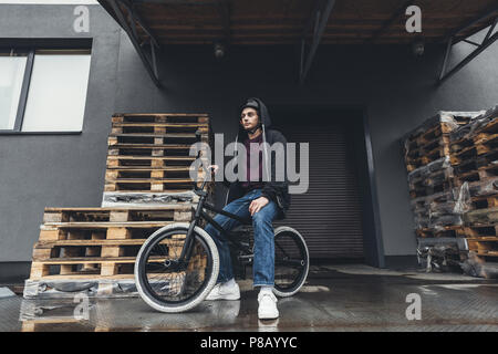 full length view of young man in helmet sitting on bmx bicycle and looking away on street Stock Photo