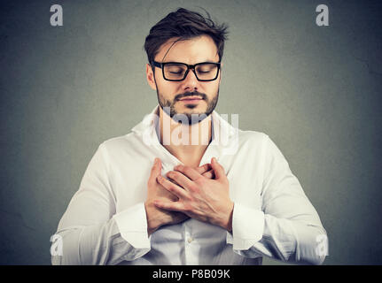 Faithful man with eyes closed keeps hands on chest near heart, shows kindness, expresses sincere emotions, being kind hearted. Body language feelings  Stock Photo