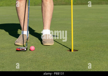 Pink golf ball by flag and hole on putting green Stock Photo