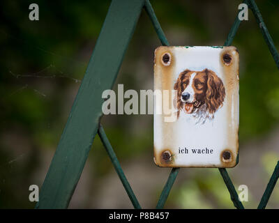 Metal sign with dog saying 'I watch out' on a green fence Stock Photo