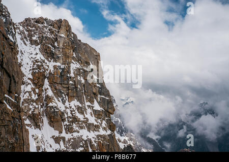 view of rocky slope with snow against clouds in sky, Ala Archa National Park, Kyrgyzstan Stock Photo