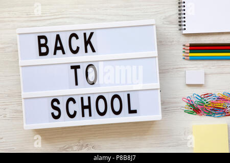 'Back to school' word on lightbox, accessories for study over white wooden surface, from above. Top view, overhead. Stock Photo