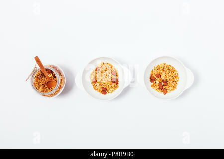 Two bowls and jar filled with oat muesli on white table, view from above. Flat lay minimal composition of homemade nut granola breakfast for couple. Stock Photo
