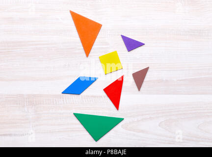 Colored geometric pieces of puzzle like triangles, square and parallelogram, are scattered on a light wooden background Stock Photo