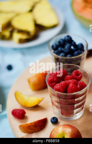 tasty healthy eating vegetarian vegan detox breakfast with fresh seasonal fruits and berries served on chopping board over pastel blue background Stock Photo