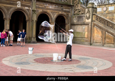 New York, NY / USA - 04.13.2018: Afro american man making a big soap bubble with bubble wand in the Central Park in NYC Stock Photo