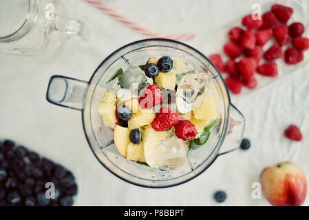 flat-lay of a blender and fresh seasonal berries and fruits over white background, cooking preparing smoothies, detox, healthy clean eating Stock Photo