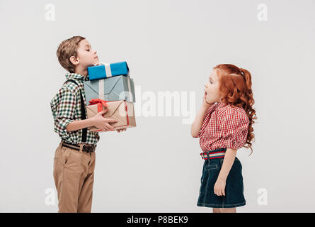 side view of boy presenting gifts to shocked little girl isolated on grey Stock Photo