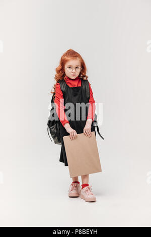 beautiful little schoolgirl in black dress with big book isolated on grey Stock Photo