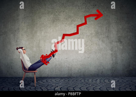 Side view of businesswoman chilling on a chair with hands behind head and red arrow growing up on gray wall background Stock Photo