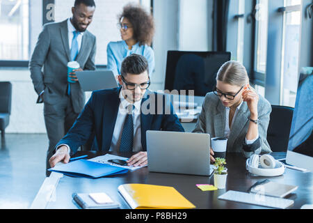 multicultural businesspeople looking at laptops in office Stock Photo