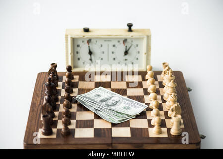 Chess clock near chess board with figures and dollar banknotes isolated on white Stock Photo
