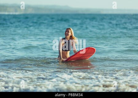 beautiful female surfer sitting on surfboard in sea Stock Photo