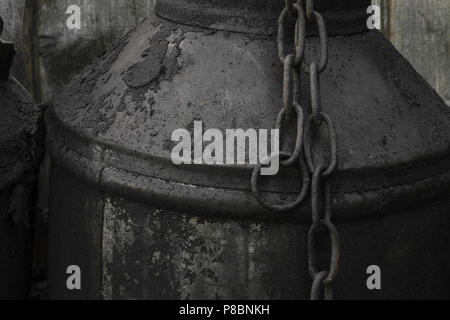 Black and oiled metal canister with the metal rusty chain in the countryside Stock Photo