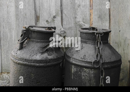 Black and oiled metal canisters in the countryside. Wooden wall in background Stock Photo