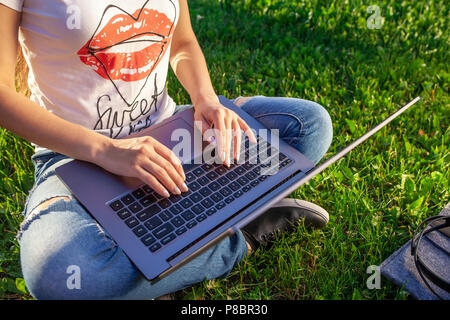 Close up hands on keyboard. Woman working on laptop pc computer in park on green grass sunshine lawn outdoors. Stock Photo