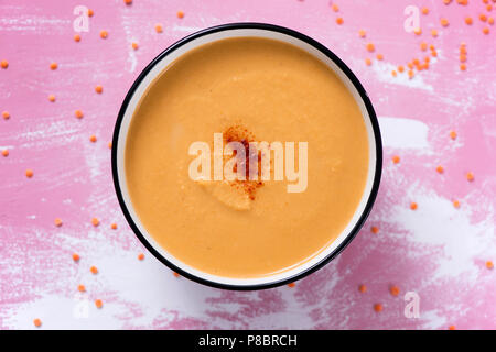 high angle view of a white ceramic bowl with a pumpkin and coconut puree sprinkled with paprika, on a rustic pink and white wooden table Stock Photo