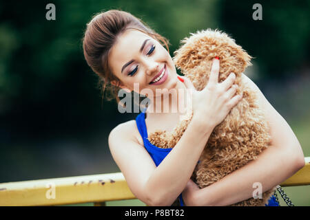 Portrait of beautiful smiling young woman with her little red poodle puppy. Stock Photo